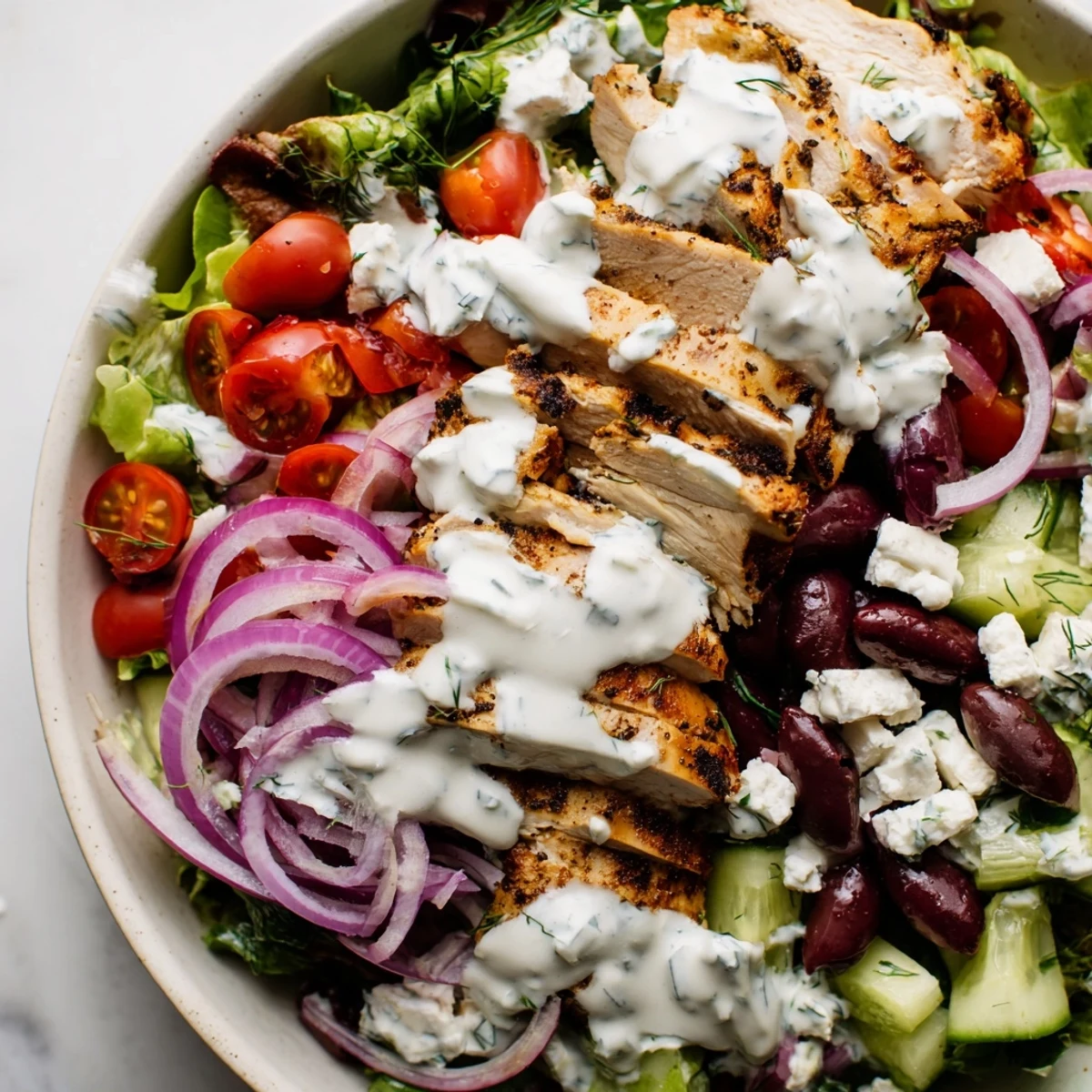 Fresh grilled chicken slices atop mixed greens with cherry tomatoes, kalamata olives, and creamy tzatziki chicken salad dressing drizzled generously over the vibrant bowl.