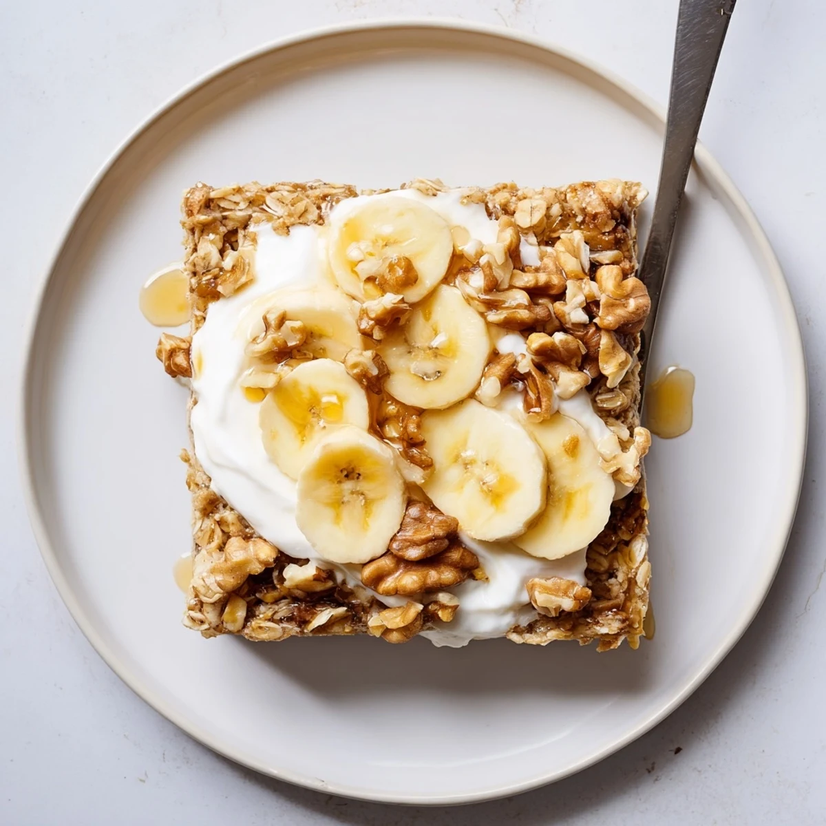 Golden banana baked oatmeal squares topped with creamy Greek yogurt and fresh banana slices