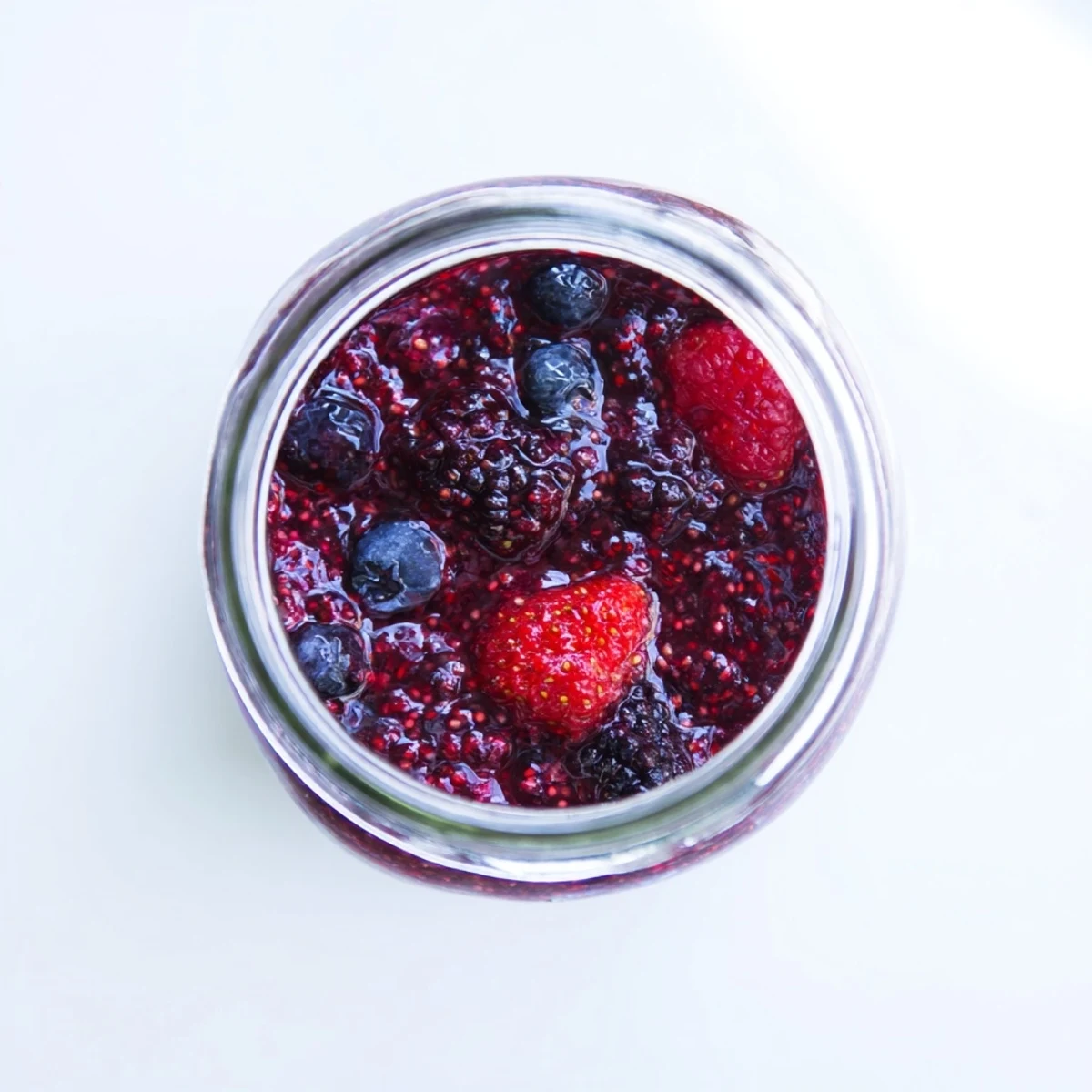 Glass jar filled with deep purple easy berry chia seed jam, chia seeds visible throughout