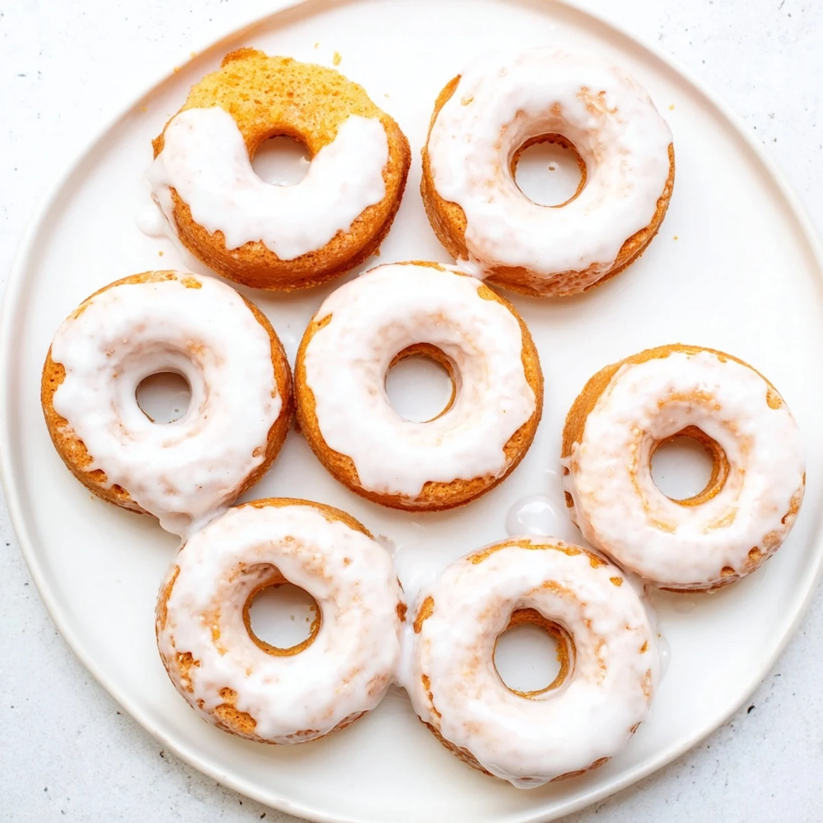 Freshly baked Greek yogurt cake donuts cooling on a wire rack with smooth white glaze dripping down the sides