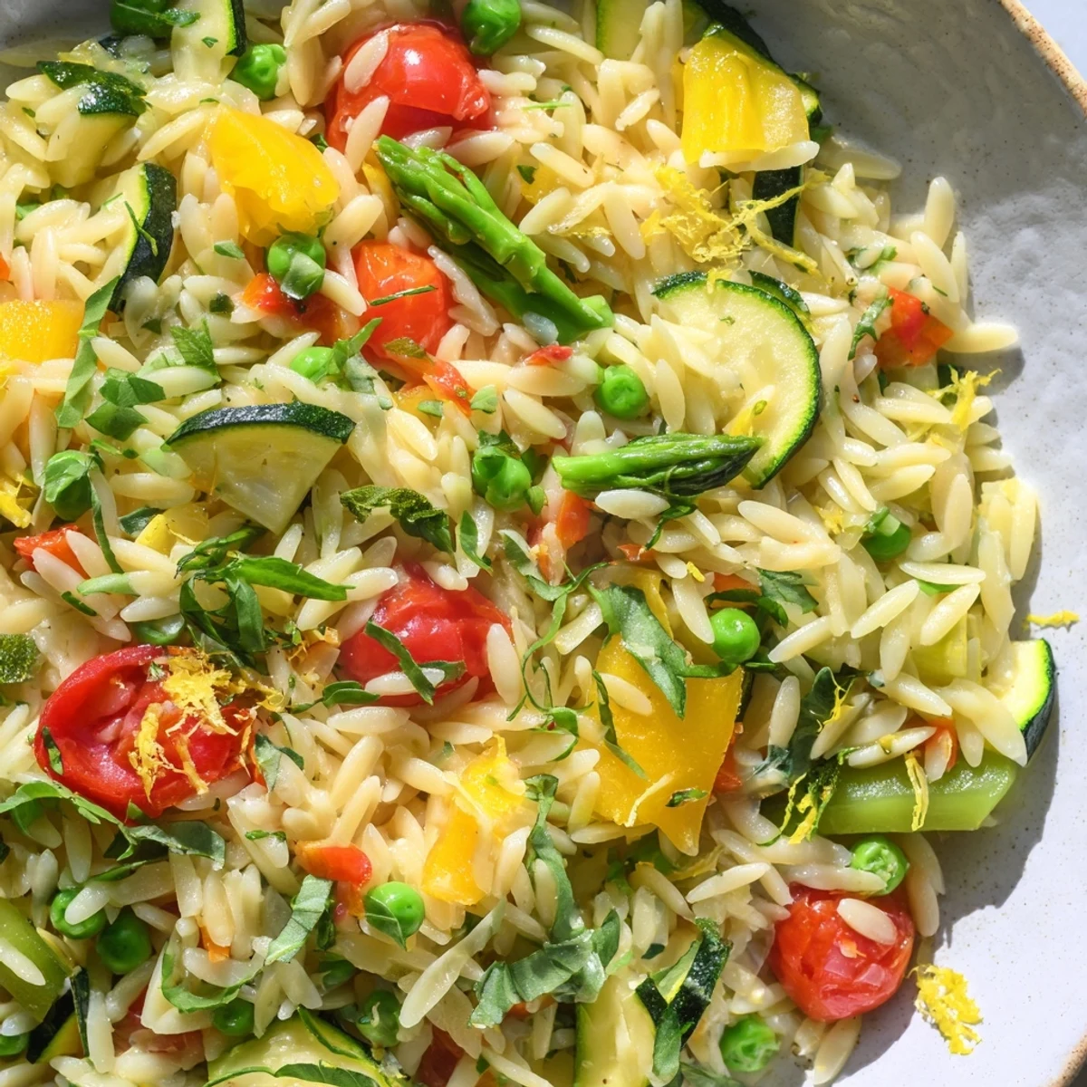 Orzo Primavera served in white bowl with bright green asparagus and cherry tomatoes