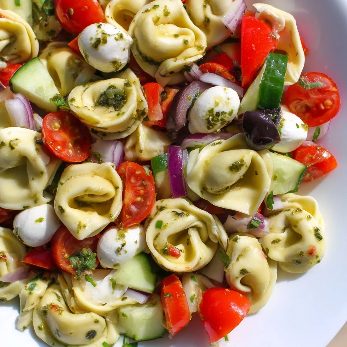 Cheese-filled tortellini pasta salad tossed with crisp vegetables and mozzarella in a white serving dish