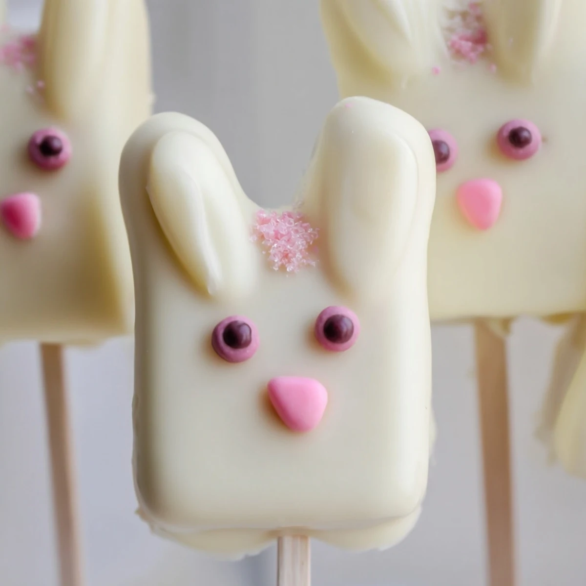 Adorable white chocolate bunny cakesicles with candy eyes and pink ears on a rustic wooden serving board