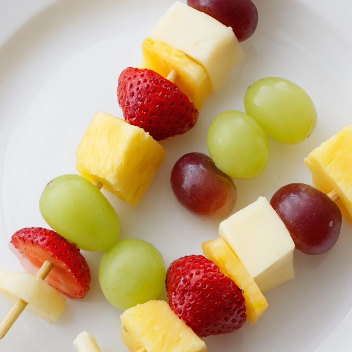 Colorful fruit and cheese kabobs arranged on platter with grapes strawberries pineapple and cheddar cubes