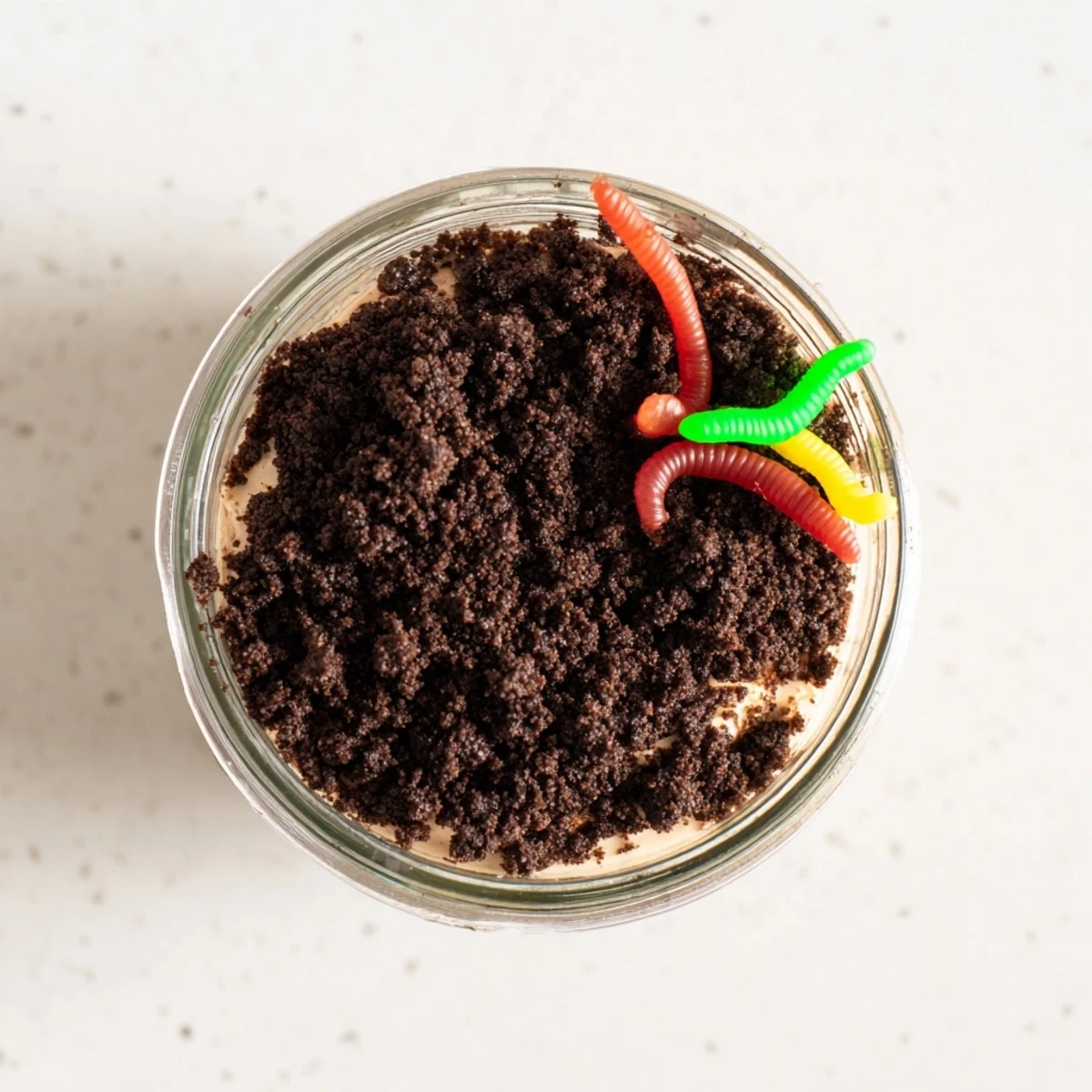 Playful dirt pudding dessert with chocolate pudding whipped topping and crawling gummy worms
