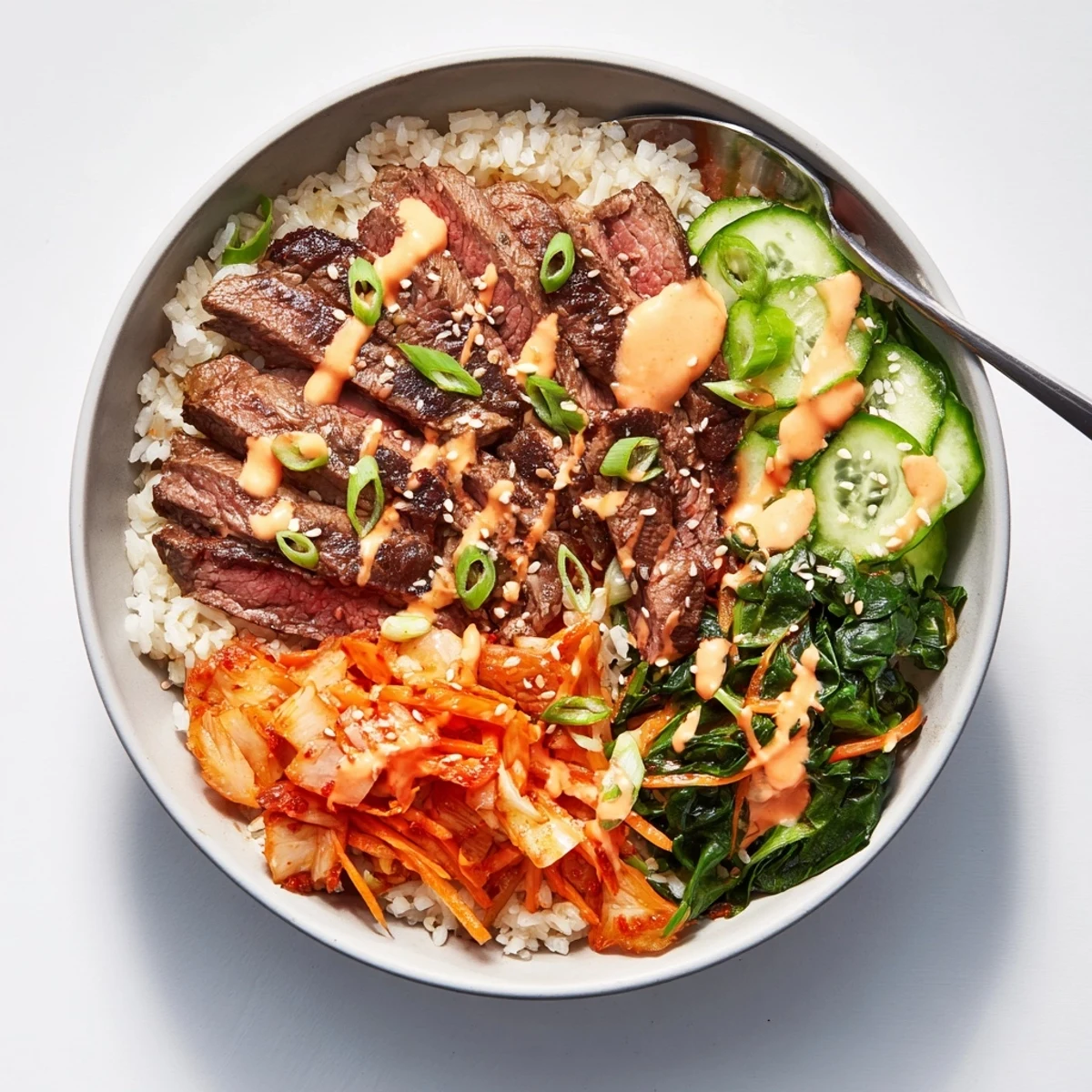Caramelized beef alongside crisp veggies and kimchi topped with creamy sriracha drizzle in Korean BBQ Steak Rice Bowls