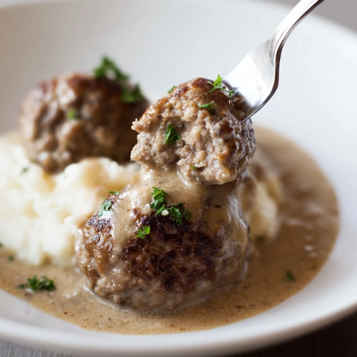 Close-up of Homemade Ikea Meatballs bathed in velvety cream sauce with lingonberry jam