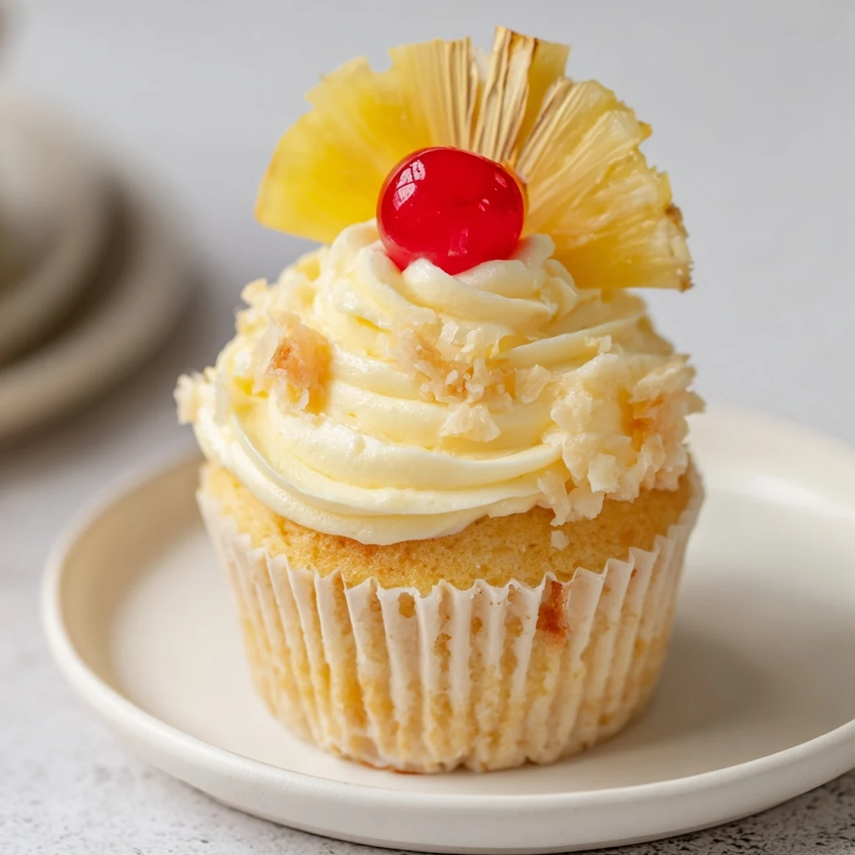 Close-up of Dole Whip Cupcakes Recipe topped with maraschino cherry and dried pineapple.