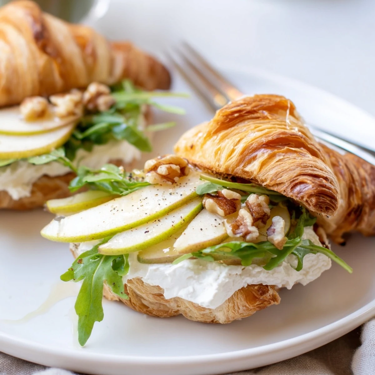 Flaky Apple Goat Cheese Croissant Sandwich topped with arugula and cracked pepper.