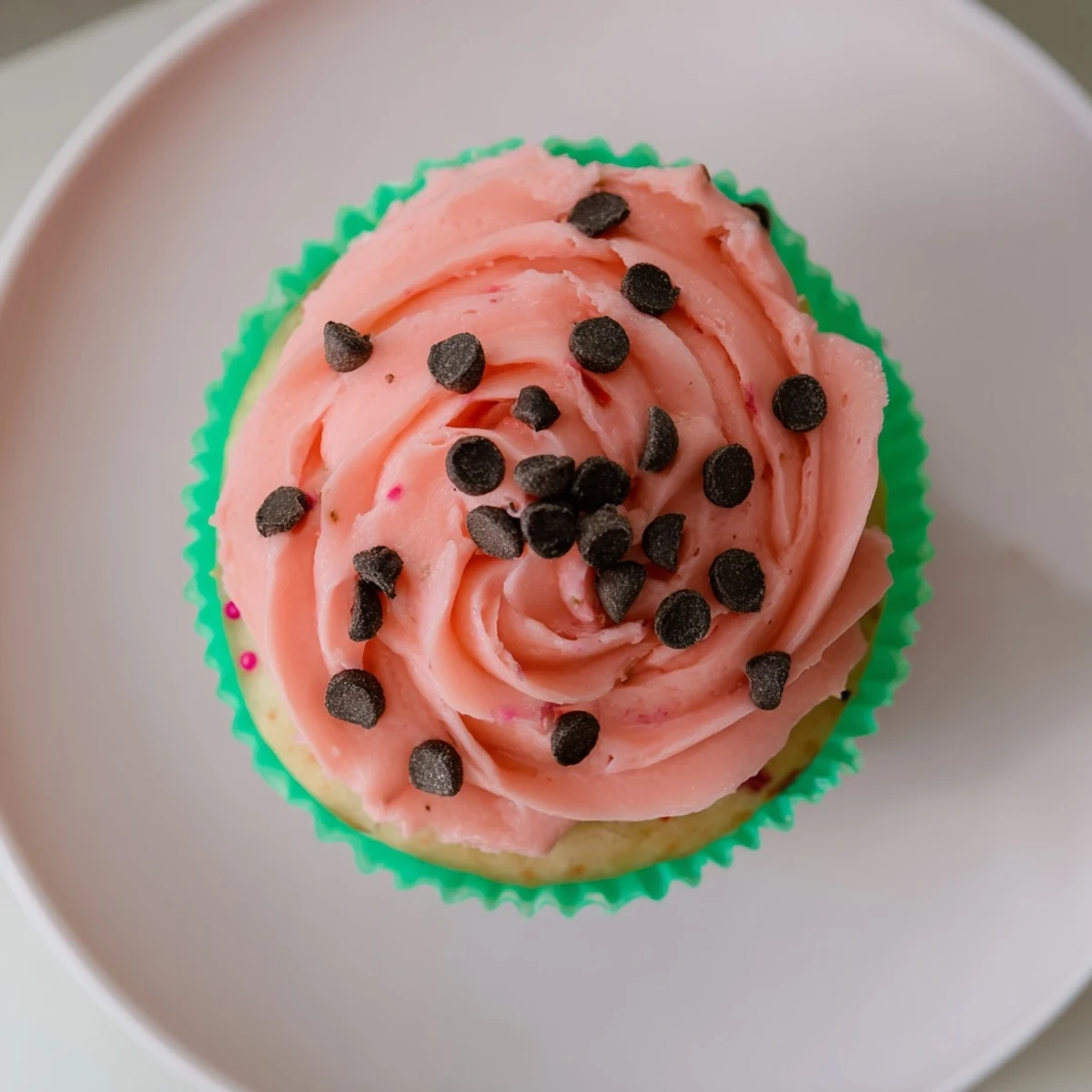 Moist watermelon cupcakes topped with pink watermelon-infused frosting and chocolate chip seeds on a white plate