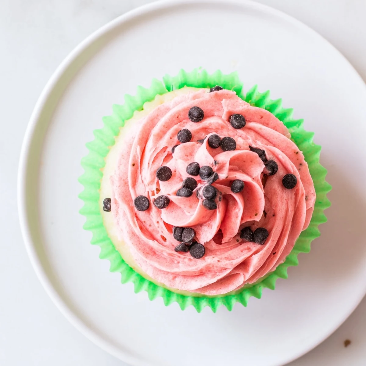Pink frosted watermelon cupcakes decorated with mini chocolate seeds arranged on a wooden serving board for summer