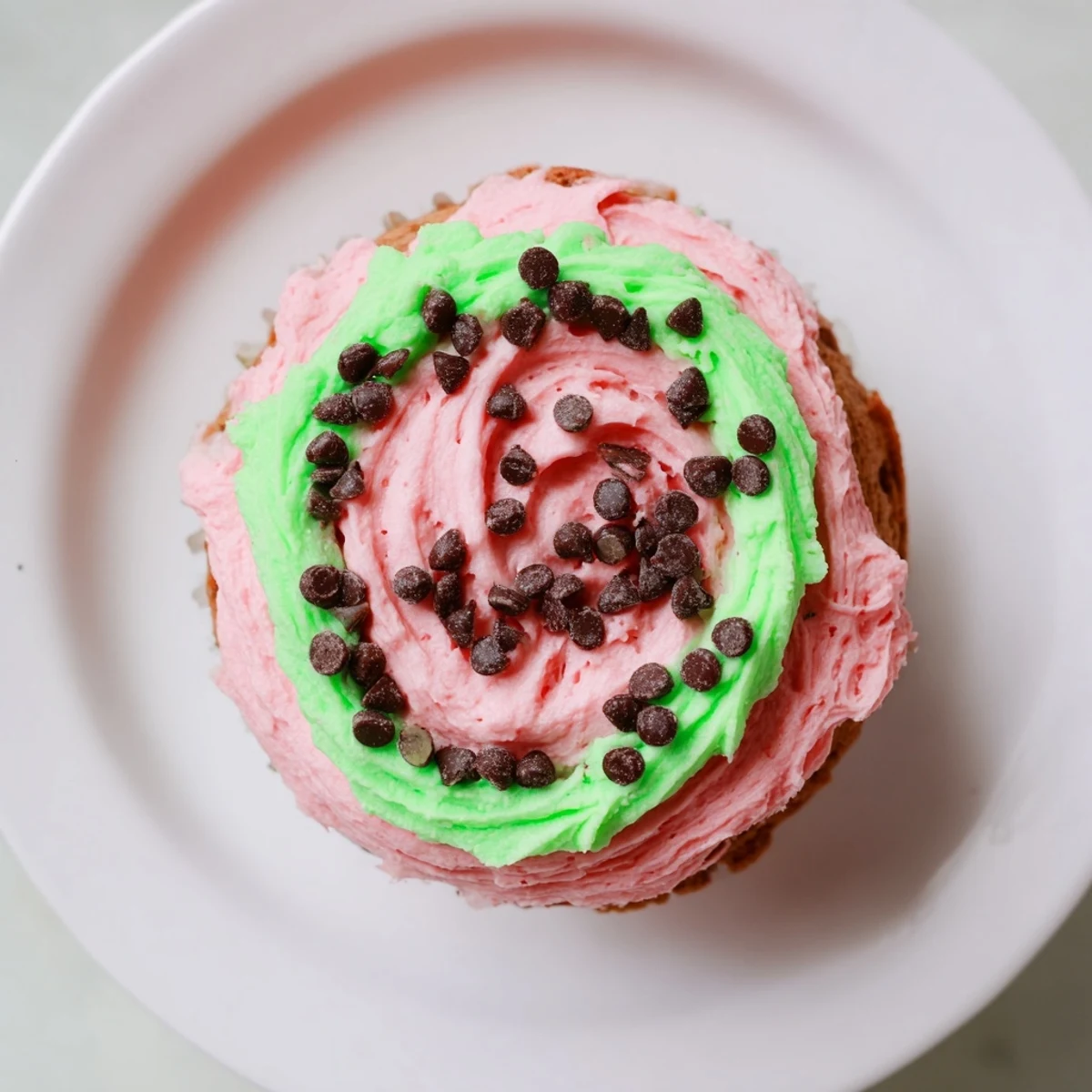 Freshly baked watermelon cupcakes with creamy pink buttercream frosting and chocolate seed accents on a decorative platter
