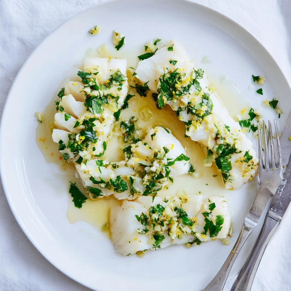 Flaky white cod topped with melting garlic butter and bright lemon zest on a white plate