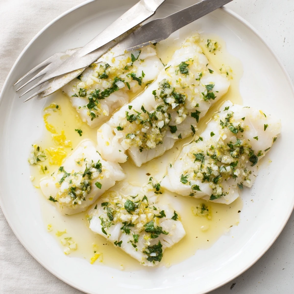 Tender lemon garlic butter cod plated with sauce and garnished with chopped parsley and lemon wedges