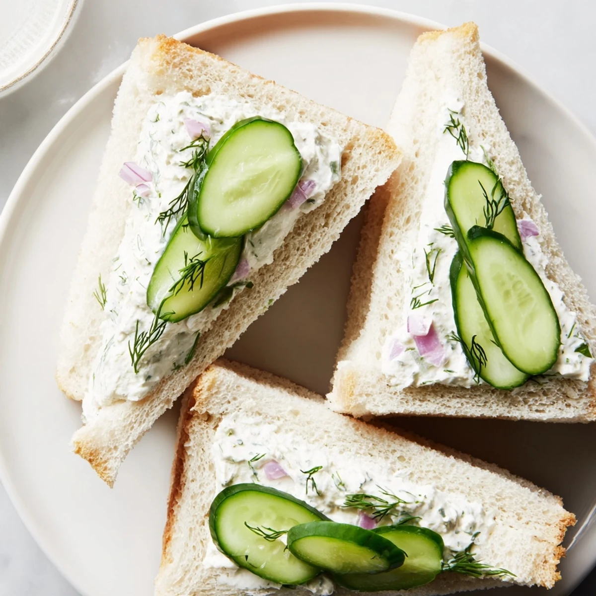 Creamy cucumber salad sandwiches layered with fresh dill spread on soft white bread triangles