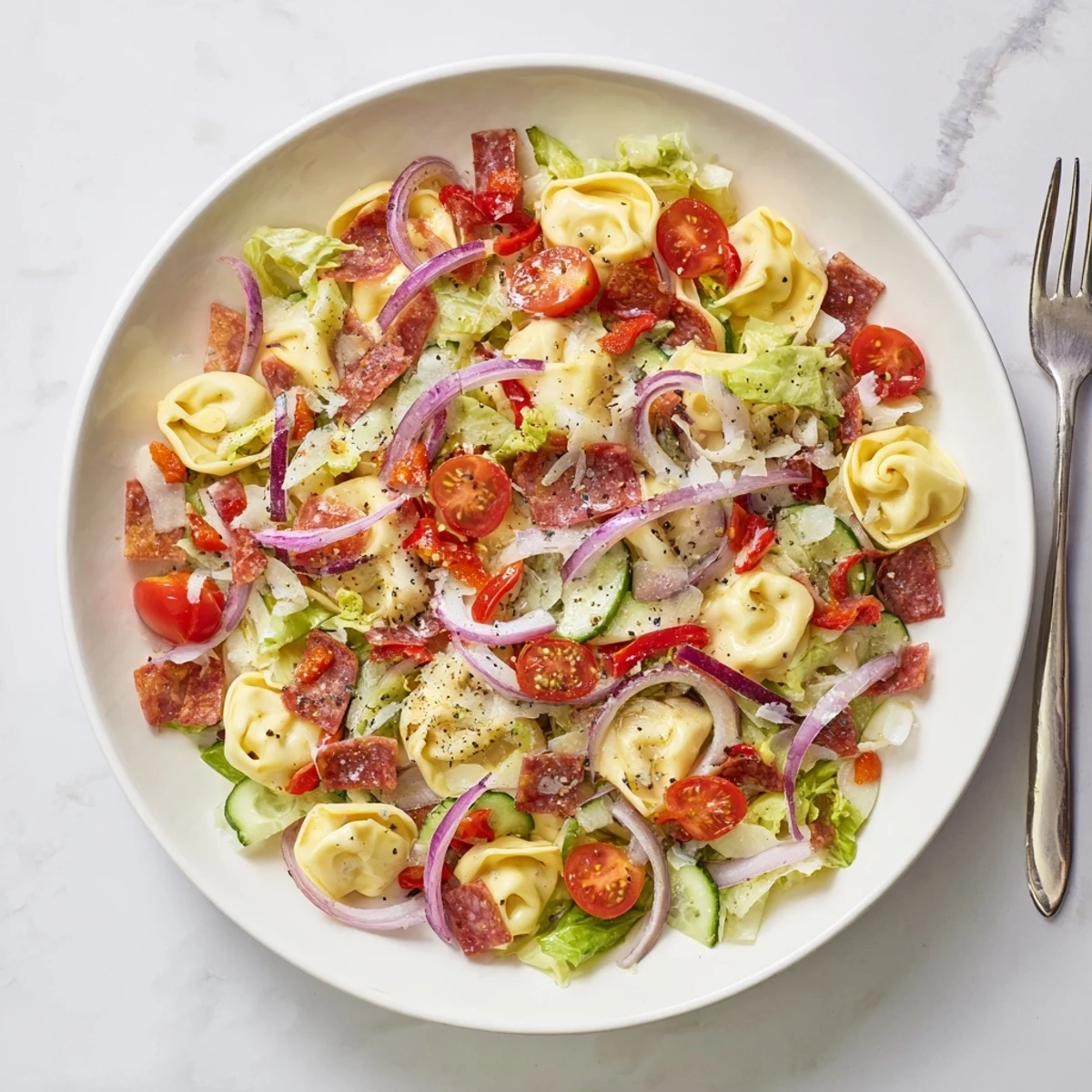 Colorful fresh grinder tortellini salad bowl with cheese tortellini, crisp vegetables, provolone, and zesty Italian dressing garnished with grated Parmesan