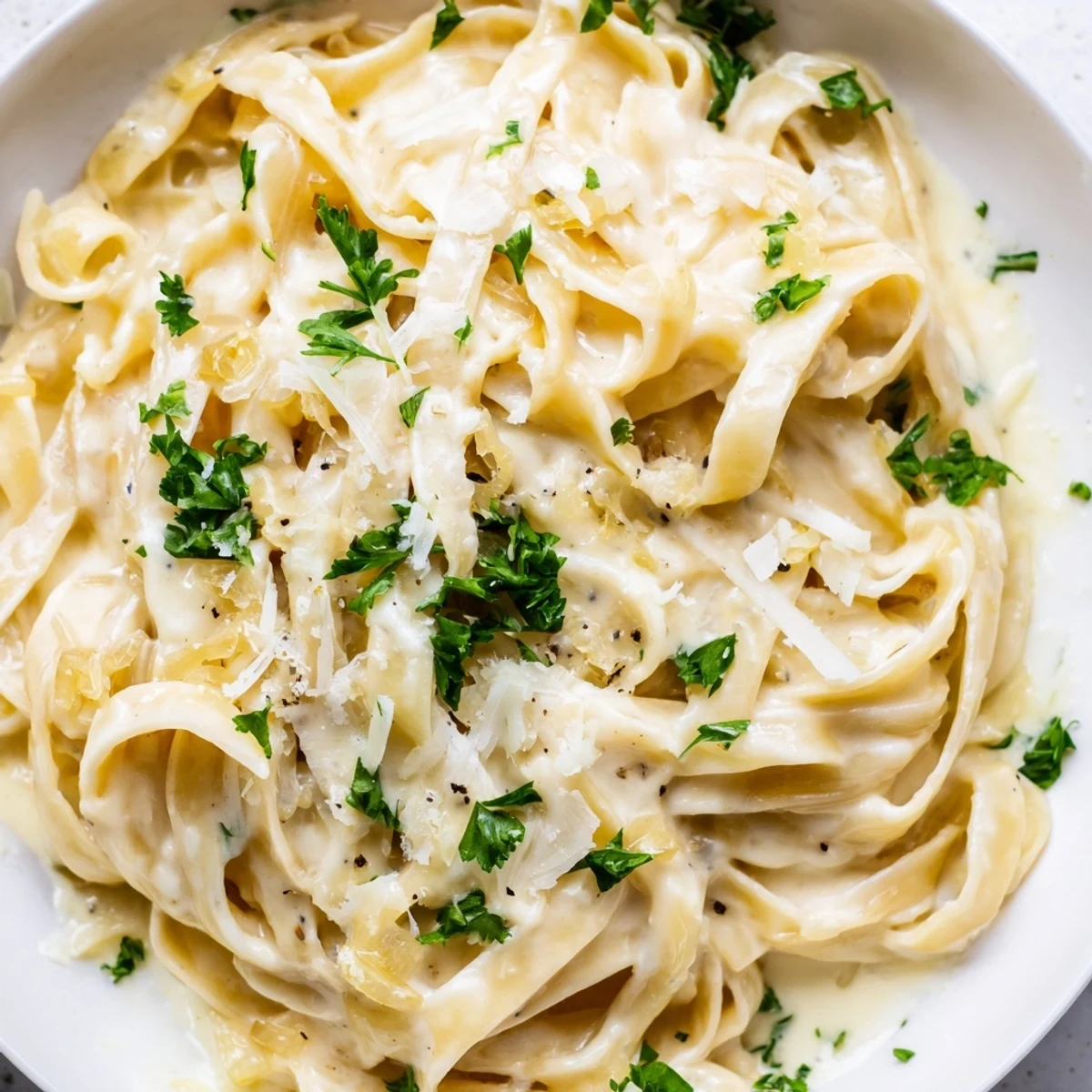Twirled fettuccine noodles coated in velvety caramelized onion cream pasta sauce with grated Parmesan