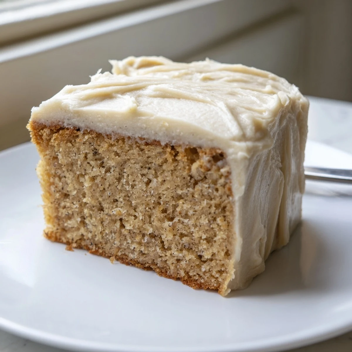 Golden slice of brown butter banana cake piled high with thick cream cheese frosting on a rustic plate