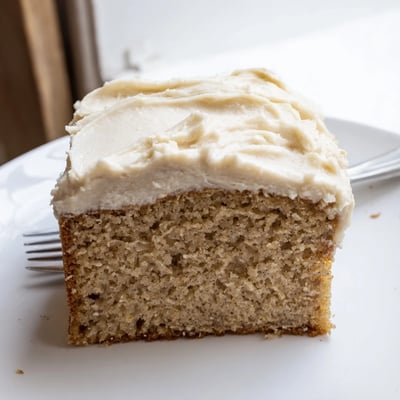 Creamy swirls of frosting top a tender brown butter banana cake garnished with ripe banana rounds
