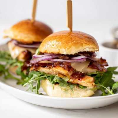 Crispy bacon and sticky maple chicken bacon sliders garnished with fresh green arugula.